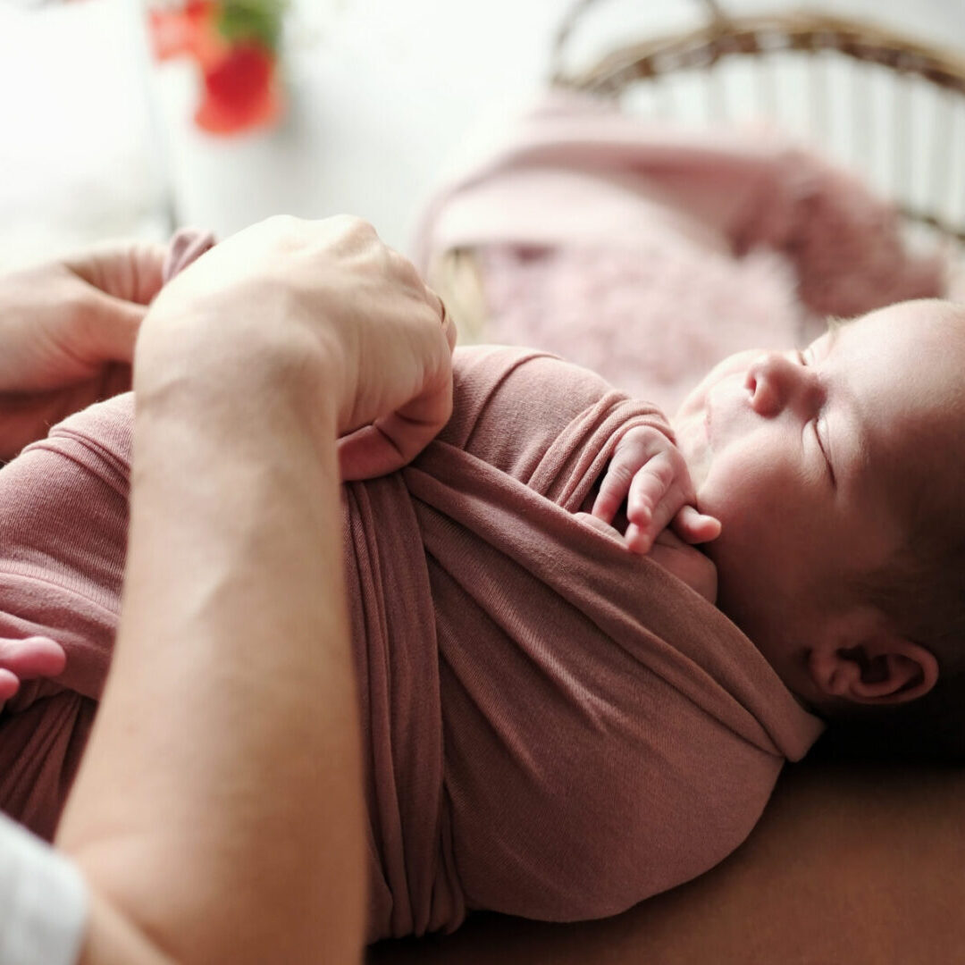 Newborn Photographer Swaddles The Baby In A Blanket During A Photoshoot
